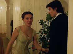 a man and woman in formal wear standing next to each other near a potted plant