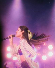 a woman with long hair standing on stage holding a microphone in front of her face