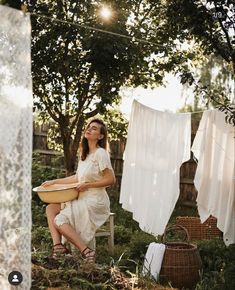 a woman sitting on a chair holding a bowl in front of clothes hanging from a line