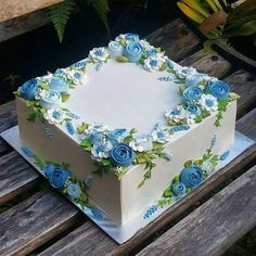 a white and blue birthday cake sitting on top of a wooden table next to flowers