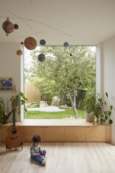 a small child sitting on the floor in front of a window looking out at a yard