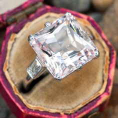 an engagement ring with a princess cut diamond in it sitting on a piece of wood