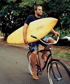 a man riding a bike with a surfboard strapped to his back