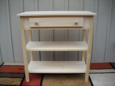 a small wooden table with two drawers on it's sides and a rug in the background