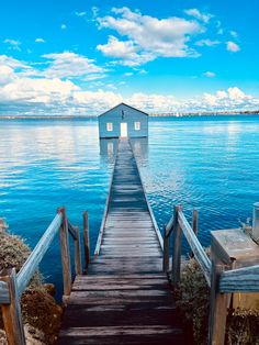 a dock leading into the water with a house on it's end and clouds in the sky