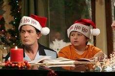 two people wearing christmas hats sitting at a table with a candle in front of them