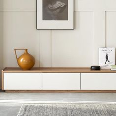 a living room with white walls and a large wooden shelf in the middle, next to a vase on top of it