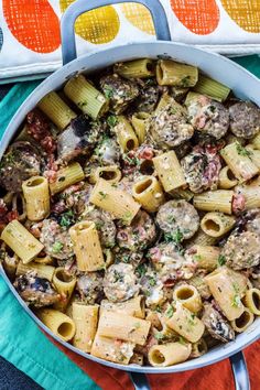 a pan filled with pasta and meatballs on top of a colorful towel next to a spoon