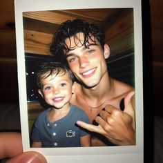 a man holding up a polaroid with a young boy pointing at the camera and smiling