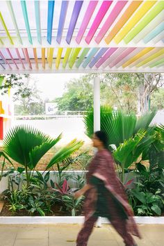 a woman walking down a sidewalk in front of plants and colorful sticks hanging from the ceiling