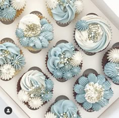 cupcakes decorated with blue and white frosting are displayed in a box on a table