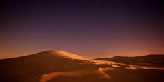 the night sky is lit up with stars above a sand dune in the sahara desert