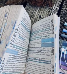 an open book sitting on top of a wooden table next to headphones and earbuds