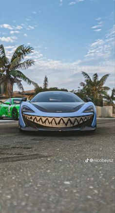 a blue sports car driving down a street next to palm trees