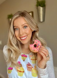 a woman holding a pink frosted donut with sprinkles