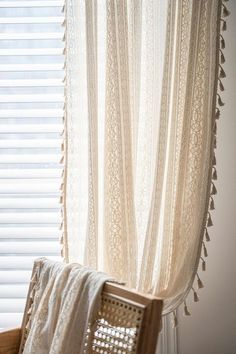 a chair sitting in front of a window with a white curtain hanging from it's side