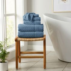 a stack of blue towels sitting on top of a wooden stool next to a bath tub