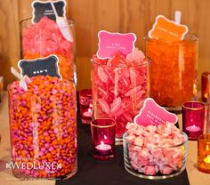 there are many candy in the glass vases on the table with candles and place cards