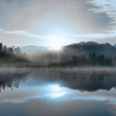 the sun shines brightly through the clouds over a lake with mountains in the background