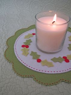 a lit candle sitting on top of a table next to a plate with holly decorations