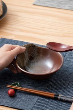 a person is holding a bowl with chopsticks next to it on a place mat