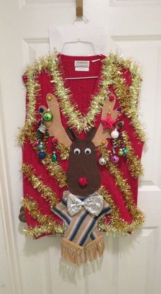 a christmas sweater hanging on the front door with reindeer decorations and tinsel around it