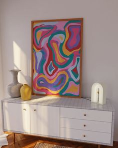 a painting is on the wall next to a dresser with drawers and vases in it