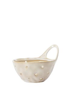 a white ceramic bowl with gold dots on the bottom and handles, sitting on a white surface