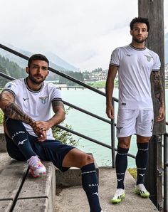 two men in soccer uniforms sitting on steps near water