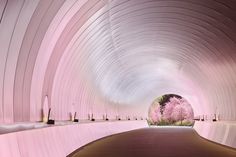 a tunnel with pink trees in the center and white walls on both sides, leading to a walkway