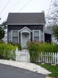 a white picket fence in front of a small house with flowers on the windows and door