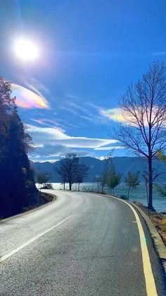 the sun shines brightly on an empty road next to water and trees with no leaves