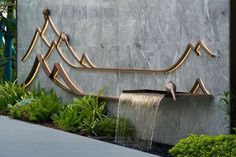 a fountain with water flowing from it in the middle of a garden area next to a building