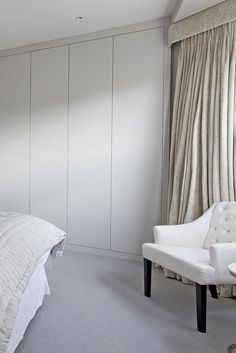 a white chair sitting in front of a bed next to a wall with curtains on it