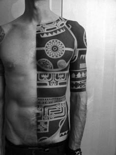 a man with tattoos on his chest standing in front of a mirror