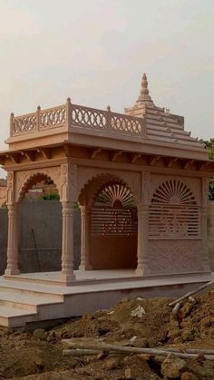 a small gazebo sitting in the middle of a dirt field next to a wall