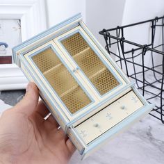 a hand holding a miniature model of a jewelry box in it's display case