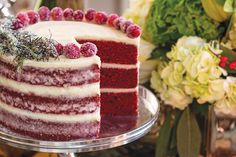 a red velvet cake with white frosting and raspberries on top is sitting on a glass platter