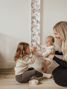 two women are playing with a baby in front of a wall hanging on the wall