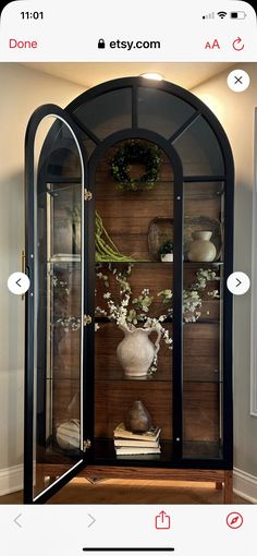 an arched glass display case with flowers and books on it in the corner of a room