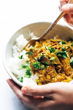 two hands holding a bowl of food with rice and meat on it, while another hand holds a spoon in the bowl