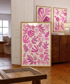 two pink and white paintings on the wall next to a wooden table in a room