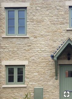 a cat sitting on the ground in front of a brick building with green doors and windows