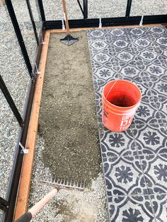 an orange bucket sitting on top of a cement floor next to a metal fence and grate