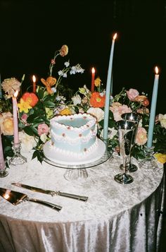 a table topped with a cake covered in frosting next to tall candles and flowers