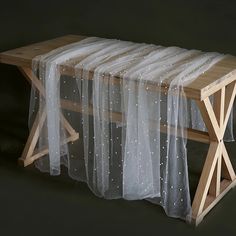 a wooden bench with white sheer curtains on it's sides and a black background