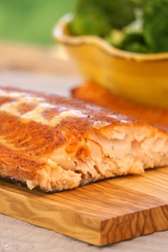 a piece of salmon on a cutting board next to a bowl of greens