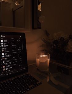 an open laptop computer sitting on top of a desk next to a candle and flowers