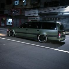 a green car driving down a street at night