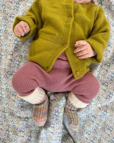 a baby doll wearing a green cardigan and pink pants laying on a floral blanket